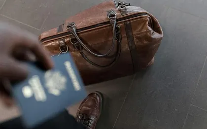A traveler holding a passport beside a packed bag